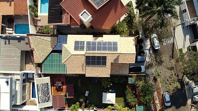 Vista aérea de uma casa com placas solares em duas águas do telhado, entre casas vizinhas