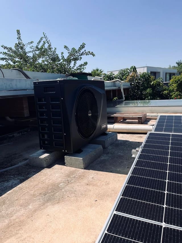 Bomba de calor de piscina sobre base de concreto em uma laje, ao lado de uma fileira de placas solares