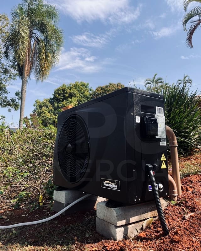 Bomba de calor Fromtherm instalada no jardim, sobre base de blocos de concreto, ligada à tubulação