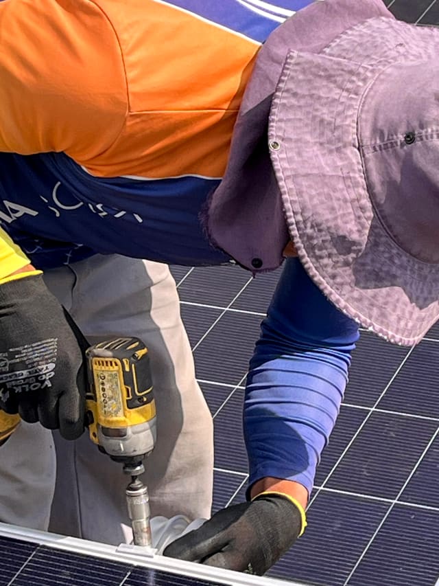 Instalador de chapéu e luvas fixando uma placa solar na estrutura com uma parafusadeira
