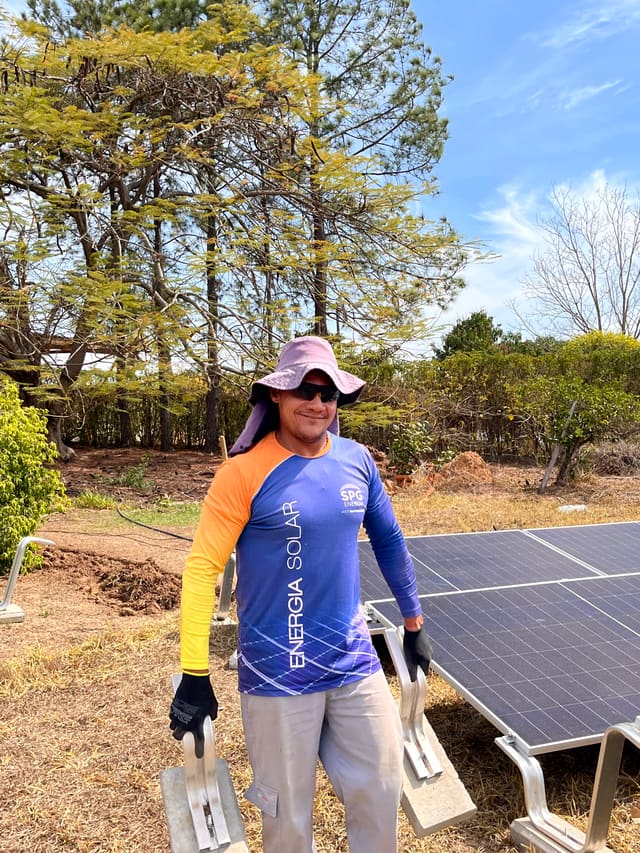 Instalador com uniforme da SPG Energia ao lado de placas solares de uma usina em solo