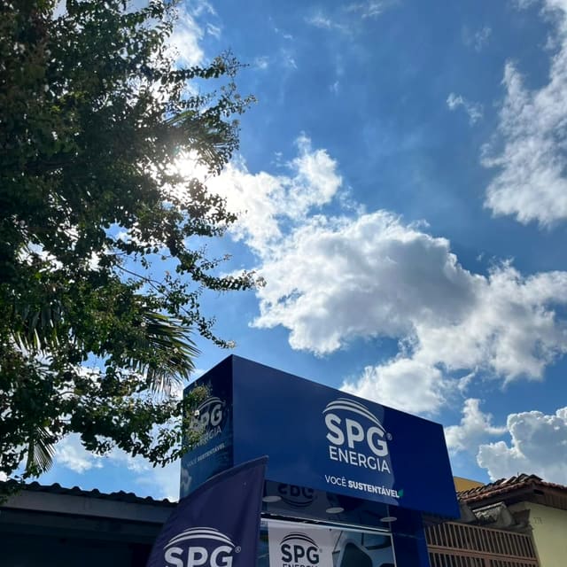 Letreiro azul da SPG Energia na fachada do escritório, com árvore e céu azul