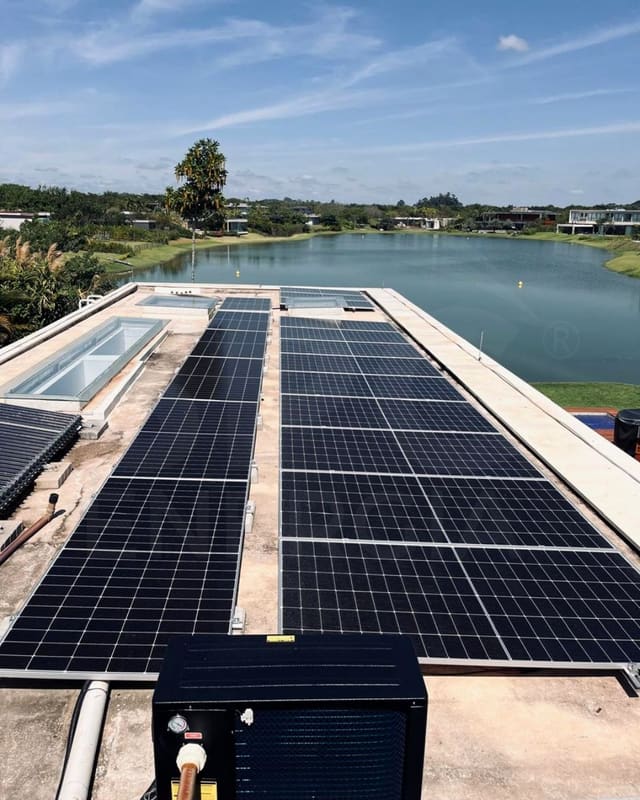 Laje com fileiras de placas solares e uma bomba de calor de piscina em primeiro plano, com um lago ao fundo