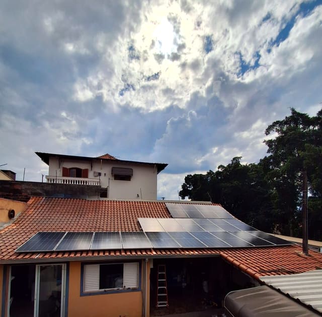 Casa com placas solares instaladas pela SPG no telhado de telha cerâmica, sob um céu de nuvens com o sol aparecendo