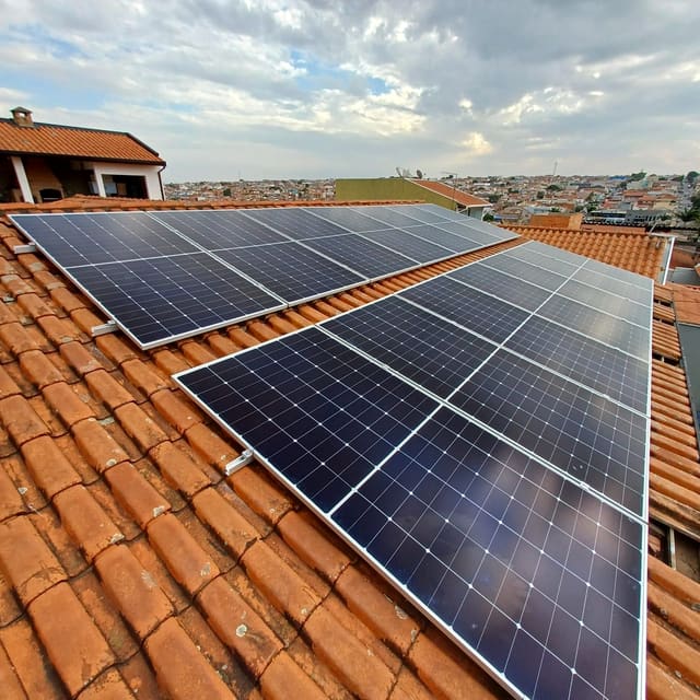 Duas fileiras de placas solares num telhado de uma água, de telha cerâmica, sob céu nublado