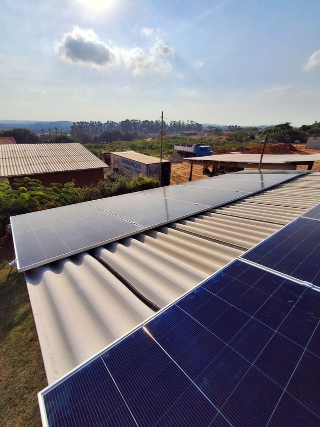 Placas solares em telhado de fibrocimento ondulado, com área rural ao fundo