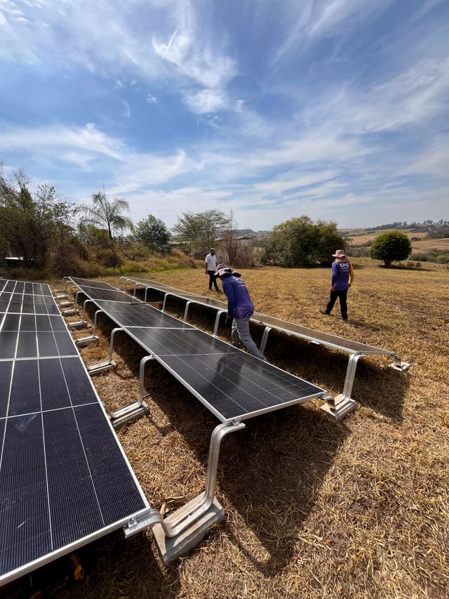 Equipe da SPG montando fileiras de placas solares sobre estruturas no solo, em terreno aberto